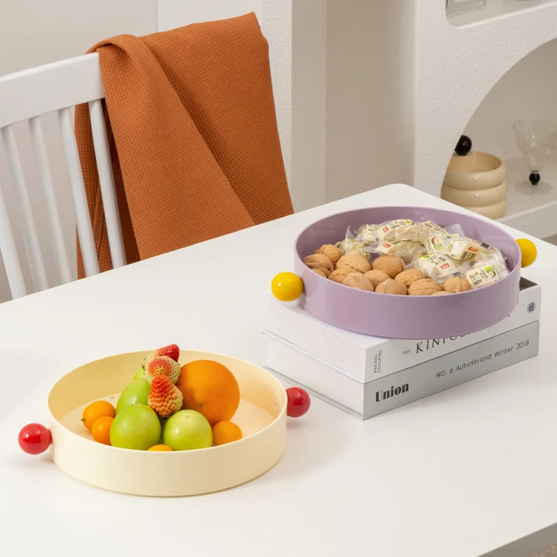 Two bowls on a table, one with fruits and the other with snacks, in a home setting.