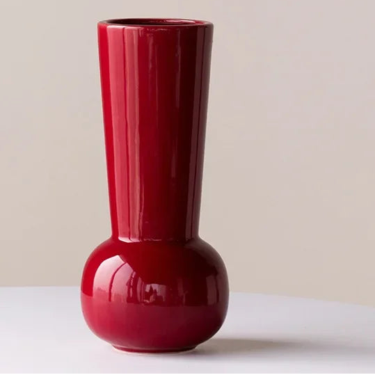 Red vase on a white surface with a beige background