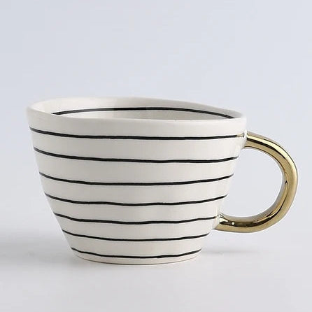 Ceramic mug with black stripes and gold handle on a light gray background