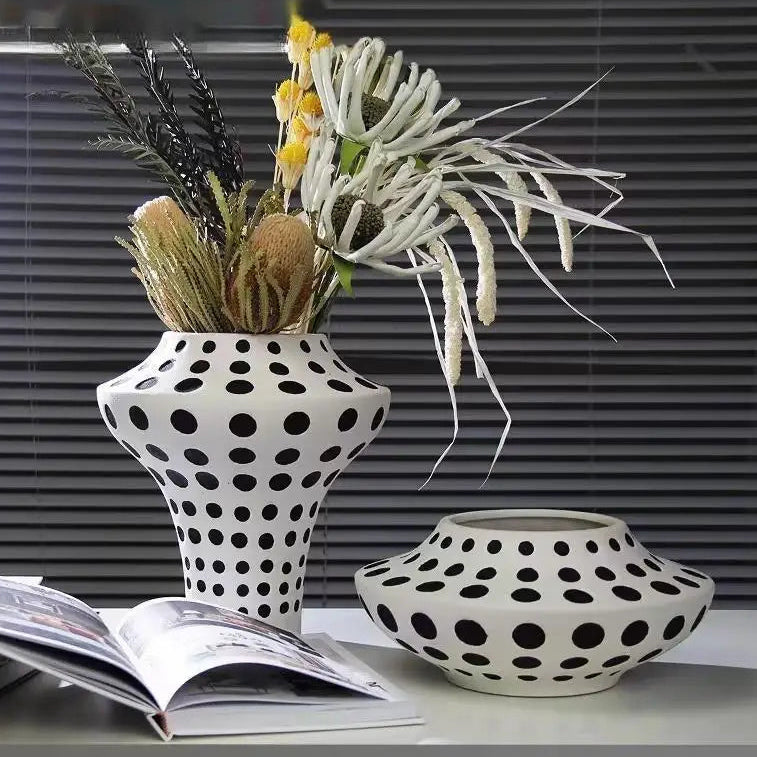 Two polka dot vases with dried flowers on a table next to an open book.