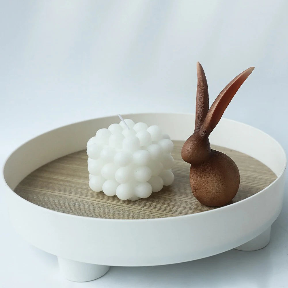 Decorative items including a white spherical object and a brown rabbit-shaped object on a wooden tray with a white base.