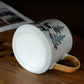 White mug with black tree design on a wooden surface