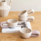 Set of ceramic cups with handles on a wooden surface with a magazine underneath.