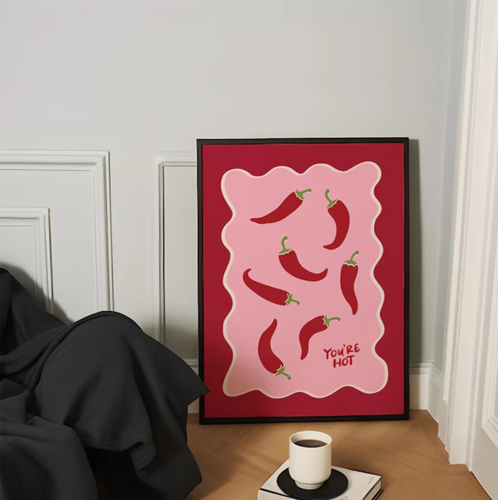 Framed artwork with red peppers on a pink background in a room setting.