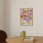 Colorful abstract art print on a wall above a wooden table with a green mug and books.