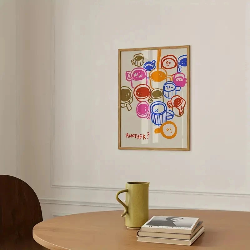 Colorful abstract art print on a wall above a wooden table with a green mug and books.