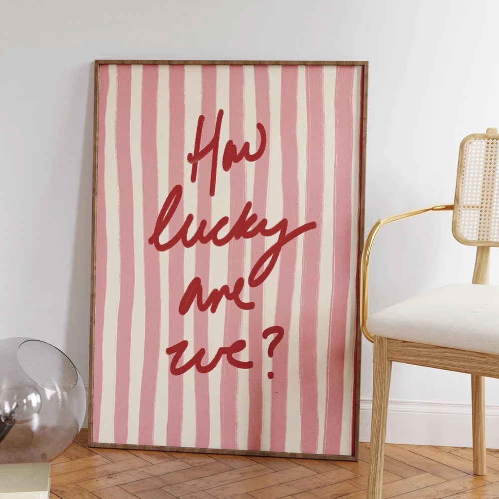 Framed artwork with pink and white stripes and red text in a room with a chair and decor items.