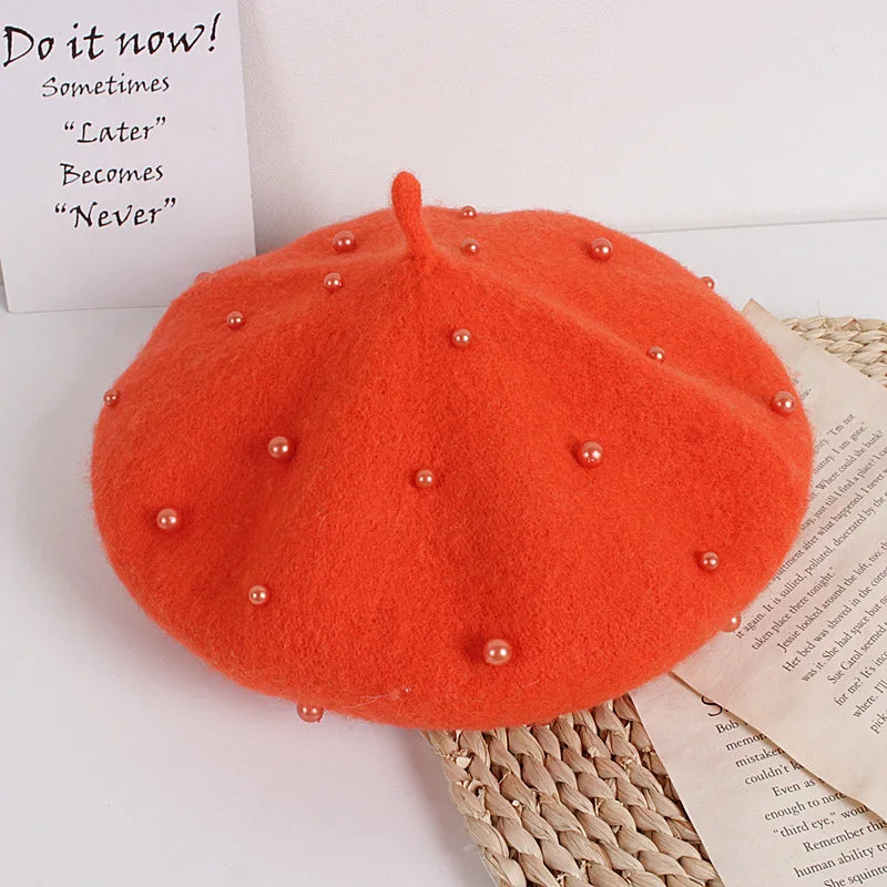 Orange beret with pearl embellishments on a white surface with text and newspaper.