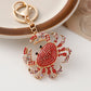 Crab-shaped keychain with red gemstones on a white surface