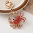 Crab-shaped keychain with red gemstones on a white surface