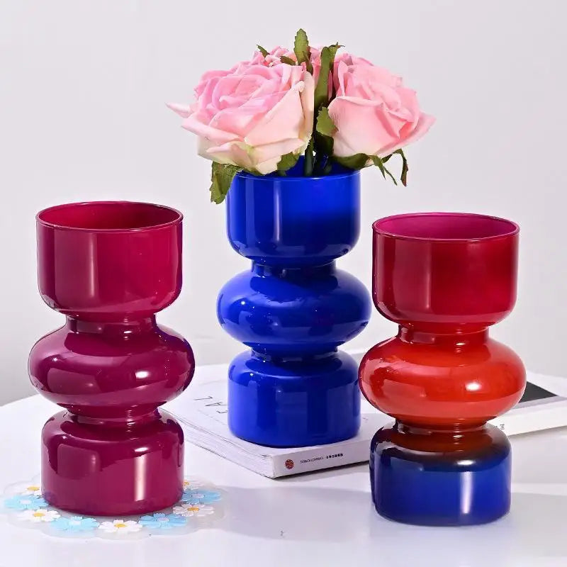 Three colorful vases with flowers on a white surface