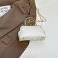 White handbag with gold chain strap on a brown fabric background