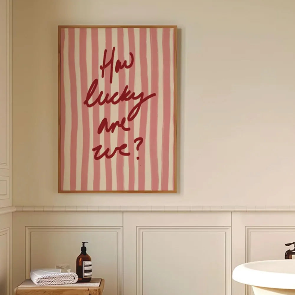 Framed artwork with 'How lucky are we?' text on a striped background in a bathroom setting.