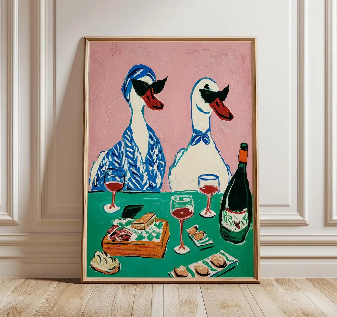 Framed artwork of two ducks with sunglasses, wine glasses, and a bottle on a pink background.