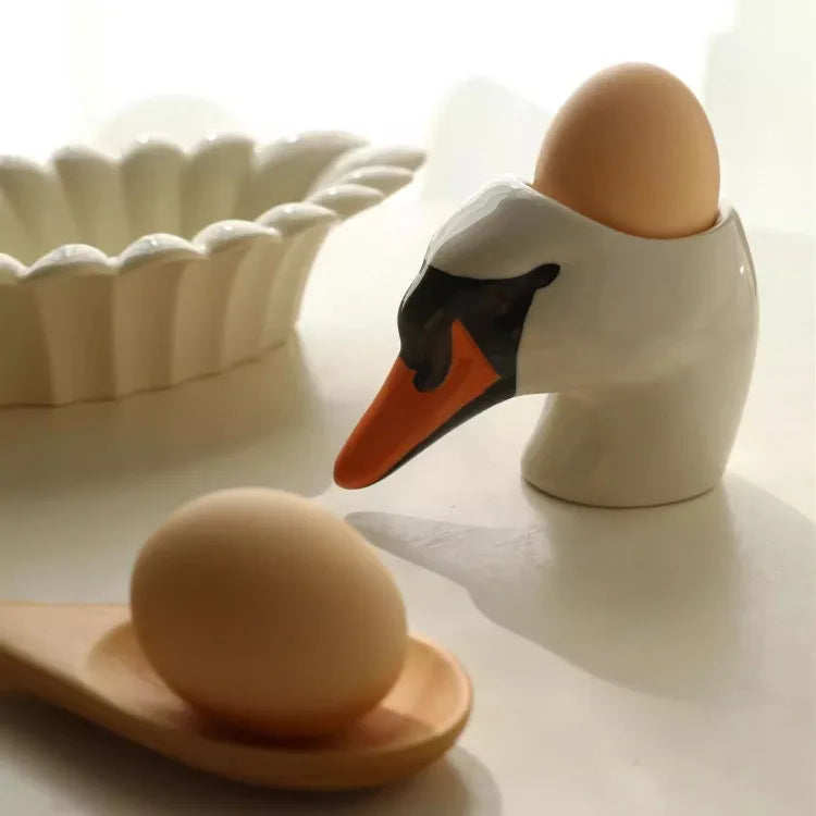 White swan-shaped egg holder with a brown egg on a light surface.