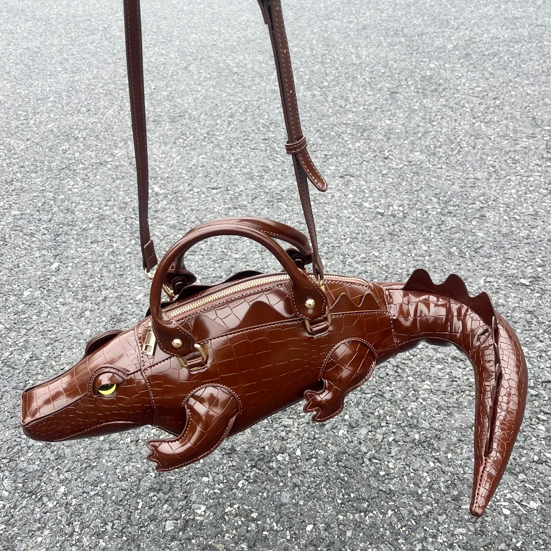 Brown alligator-shaped handbag on a gray pavement background