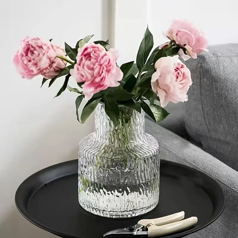 Clear glass vase with pink flowers on a black tray against a neutral background