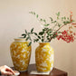 Two yellow vases with floral patterns on a wooden surface against a beige wall.