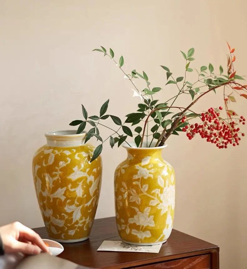 Two yellow vases with floral patterns on a wooden surface against a beige wall.