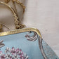 Close-up of a handbag with floral embroidery and gold frame on a light background