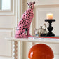 Decorative ceramic cheetah on a shelf with a candle and books in a room.