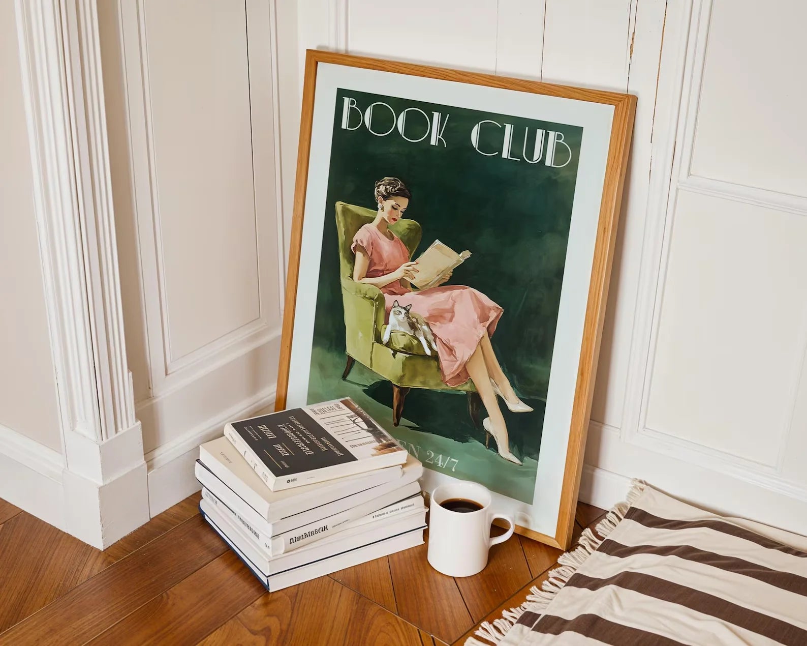 Framed poster of a woman reading with 'Book Club' text, next to stacked books and a cup on a wooden floor.