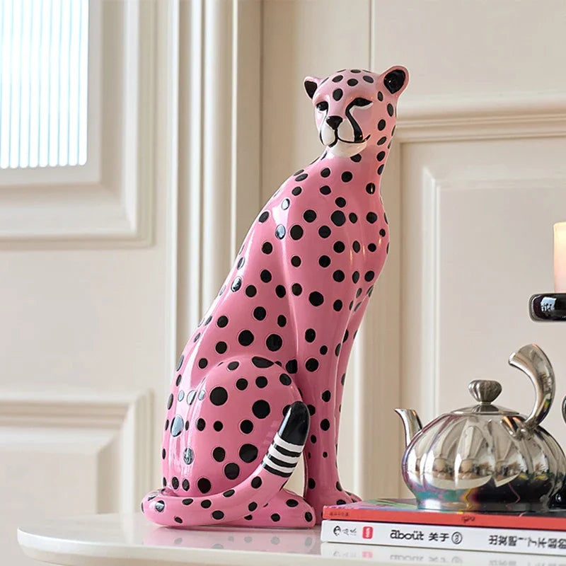 Pink and black spotted cheetah figurine on a surface with a decorative teapot and books in the background.