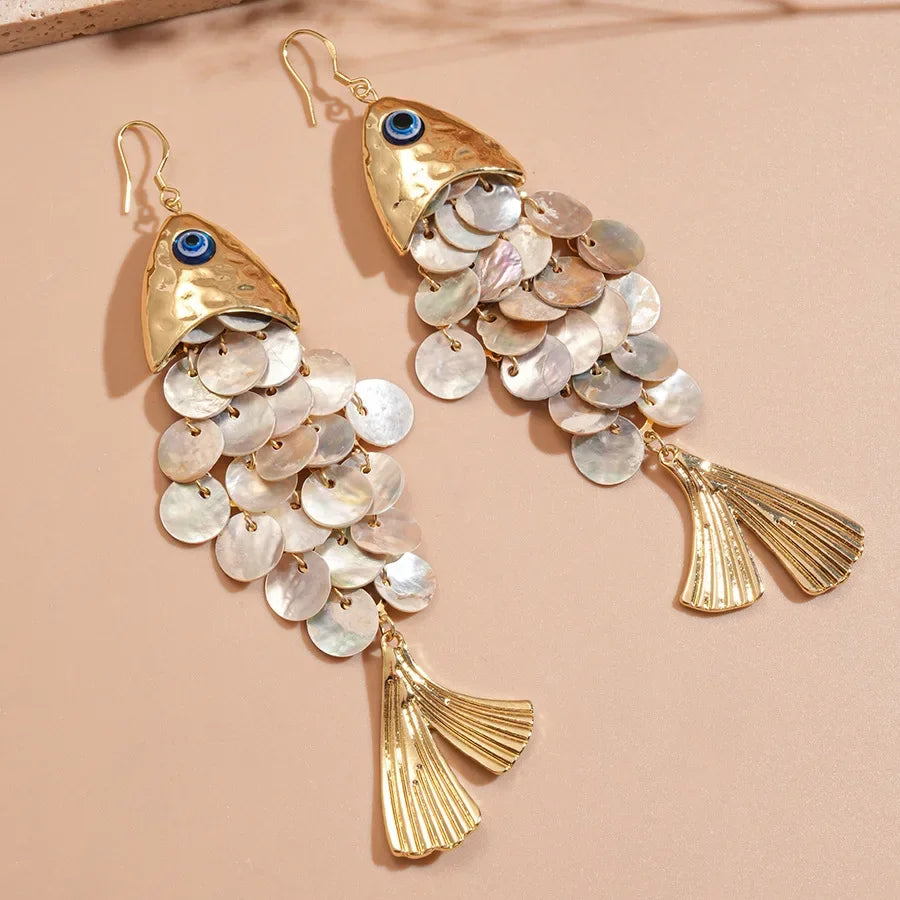 Gold fish-shaped earrings with shell accents on a beige background