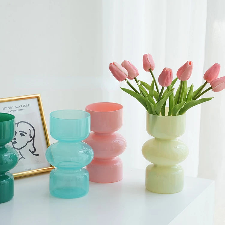 Colorful glass vases with a vase of pink tulips on a white surface.