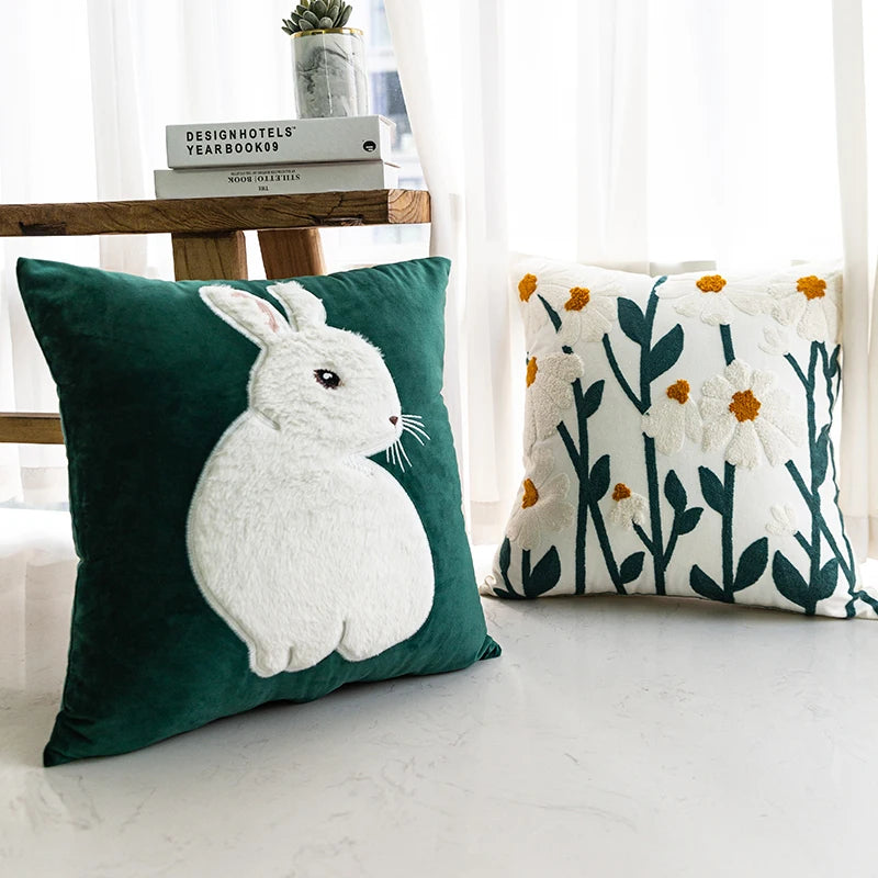 Two decorative pillows, one with a rabbit design on a green background and the other with floral pattern, on a light surface.