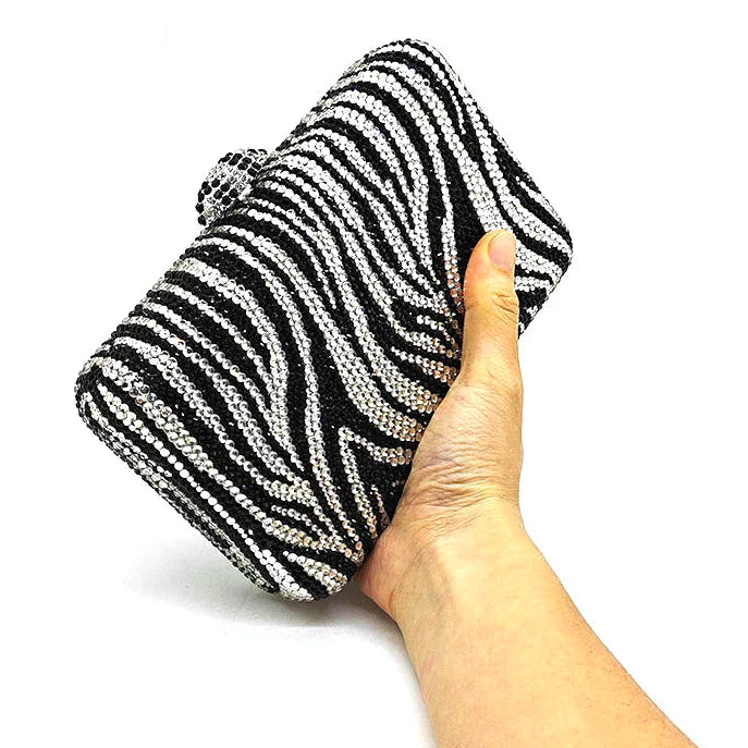 Hand holding a black and white striped clutch bag on a white background