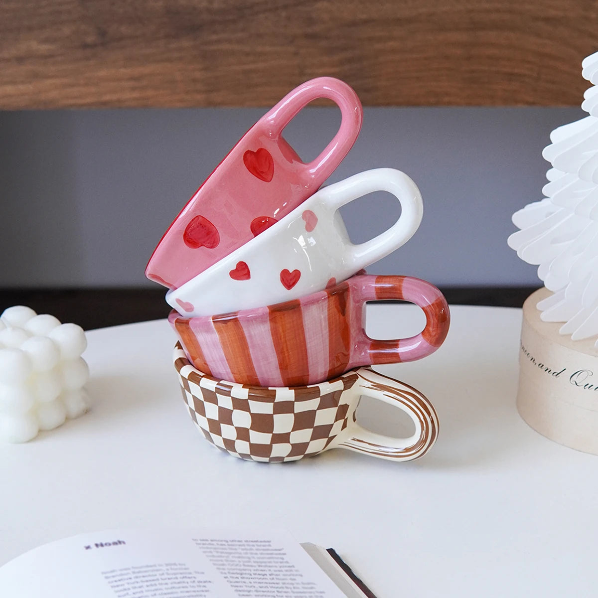 Stack of colorful ceramic cups with heart designs on a white surface.