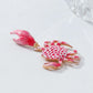 Pink crab-shaped earring on a light gray background