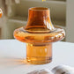 Orange glass vase on a table with yellow flowers and a magazine in the background