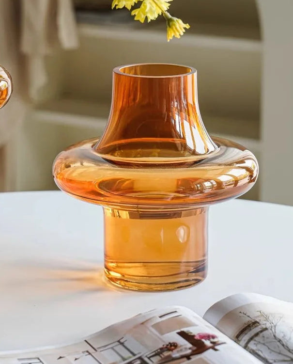 Orange glass vase on a table with yellow flowers and a magazine in the background