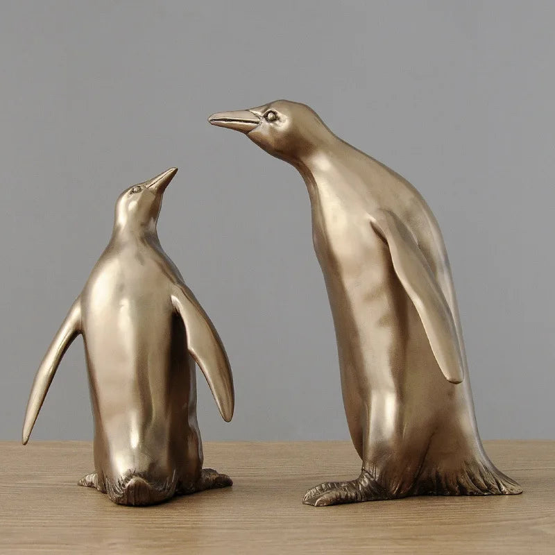 Two bronze penguin statues on a wooden surface with a gray background