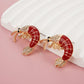 Shrimp-shaped earrings with gold and red details on a pink background