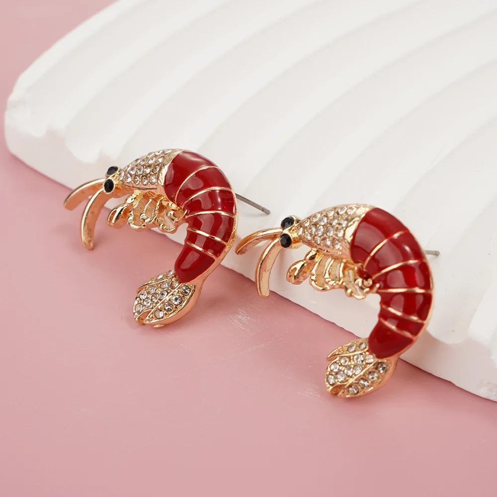 Shrimp-shaped earrings with gold and red details on a pink background