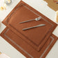 Brown placemats with cut-out patterns on a white surface with cutlery.