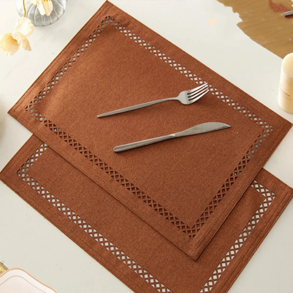Brown placemats with cut-out patterns on a white surface with cutlery.