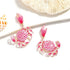 Pink crab-shaped earrings on a white background with shells.