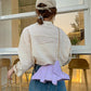 Person wearing a light-colored jacket with a purple waist bag in an indoor setting.