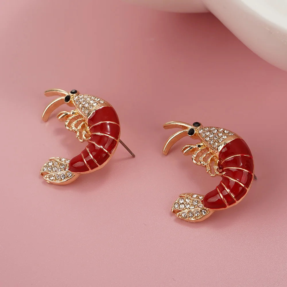 Shrimp-shaped earrings with red body and gold accents on a pink background
