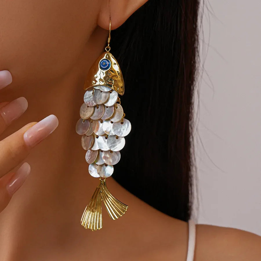 Gold fish-shaped earring with shell details worn by a person