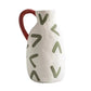 White ceramic pitcher with red handle and green abstract patterns on a white background