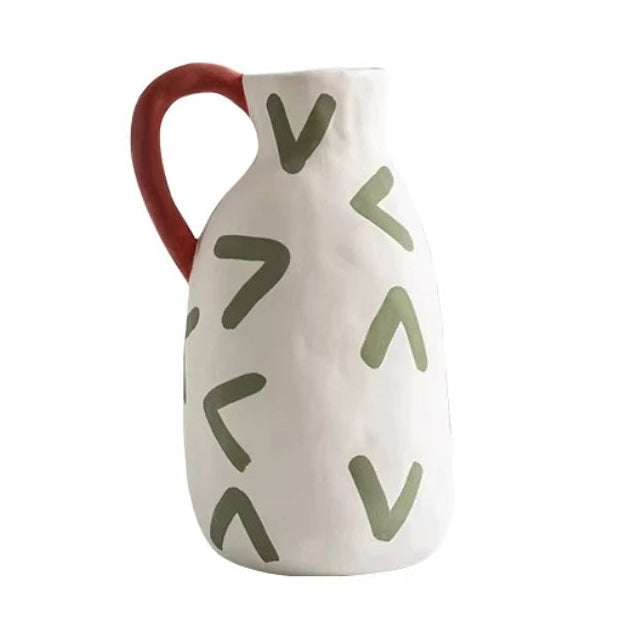 White ceramic pitcher with red handle and green abstract patterns on a white background