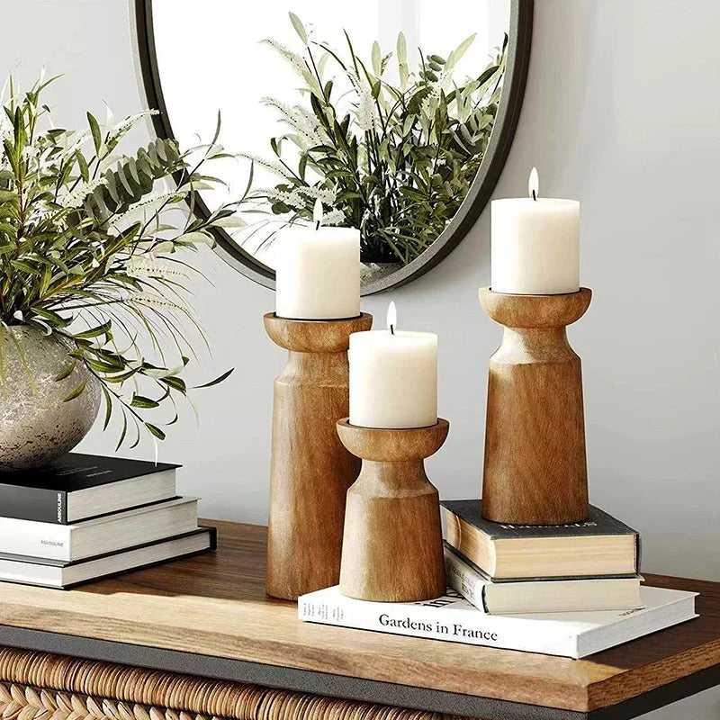 Decorative setup with wooden candle holders, candles, books, and a plant on a table.