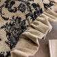 Close-up of a decorative pillow with black floral pattern and beige ruffled edge.