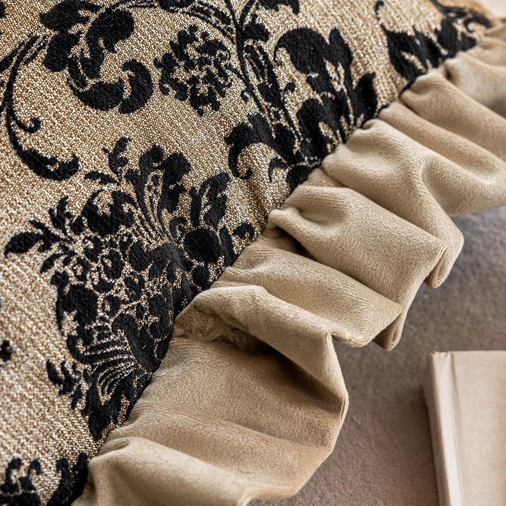 Close-up of a decorative pillow with black floral pattern and beige ruffled edge.