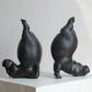 Two black ceramic sculptures of animals on a white surface with a light gray background
